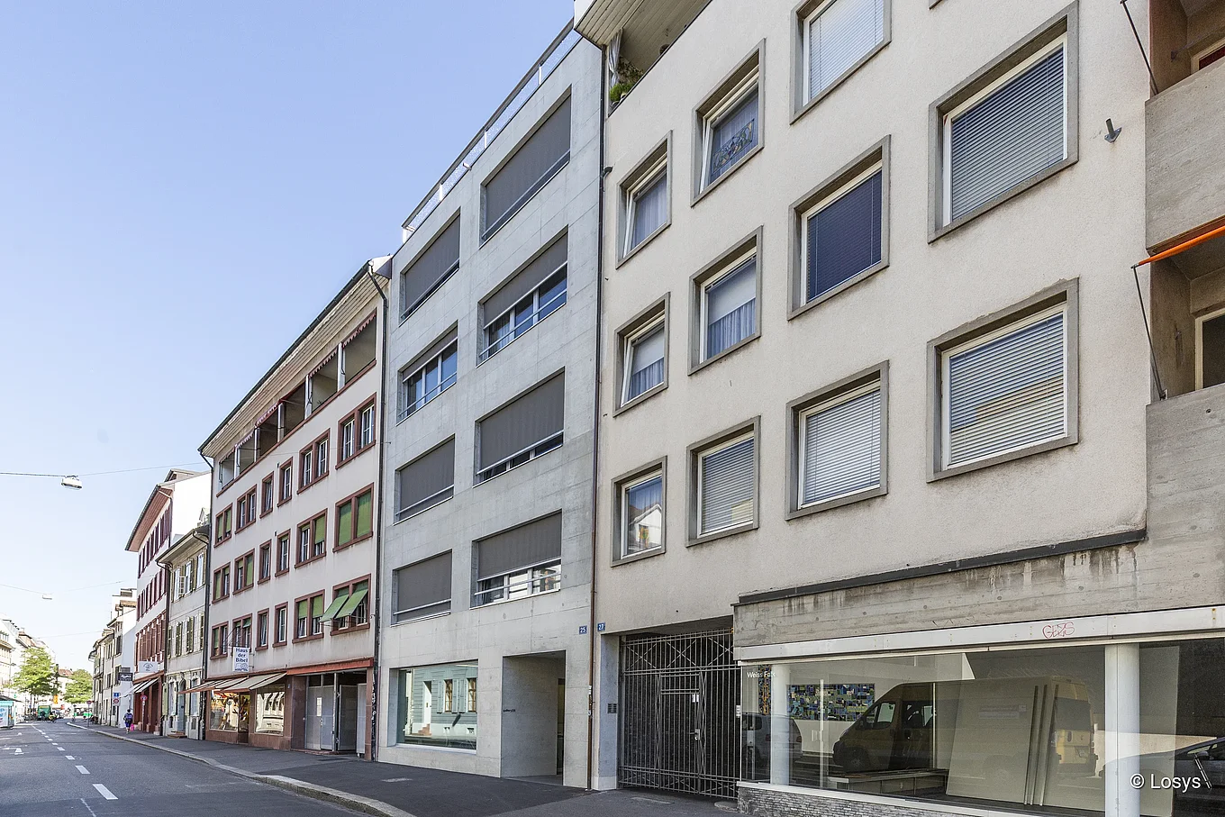Rebgasse, Basel – Straßenansicht mit Reihen mehrgeschossiger Wohn- und Geschäftshäuser, rechteckigen Fenstern, Schaufenstern, Metalltor und ruhiger Fahrbahn