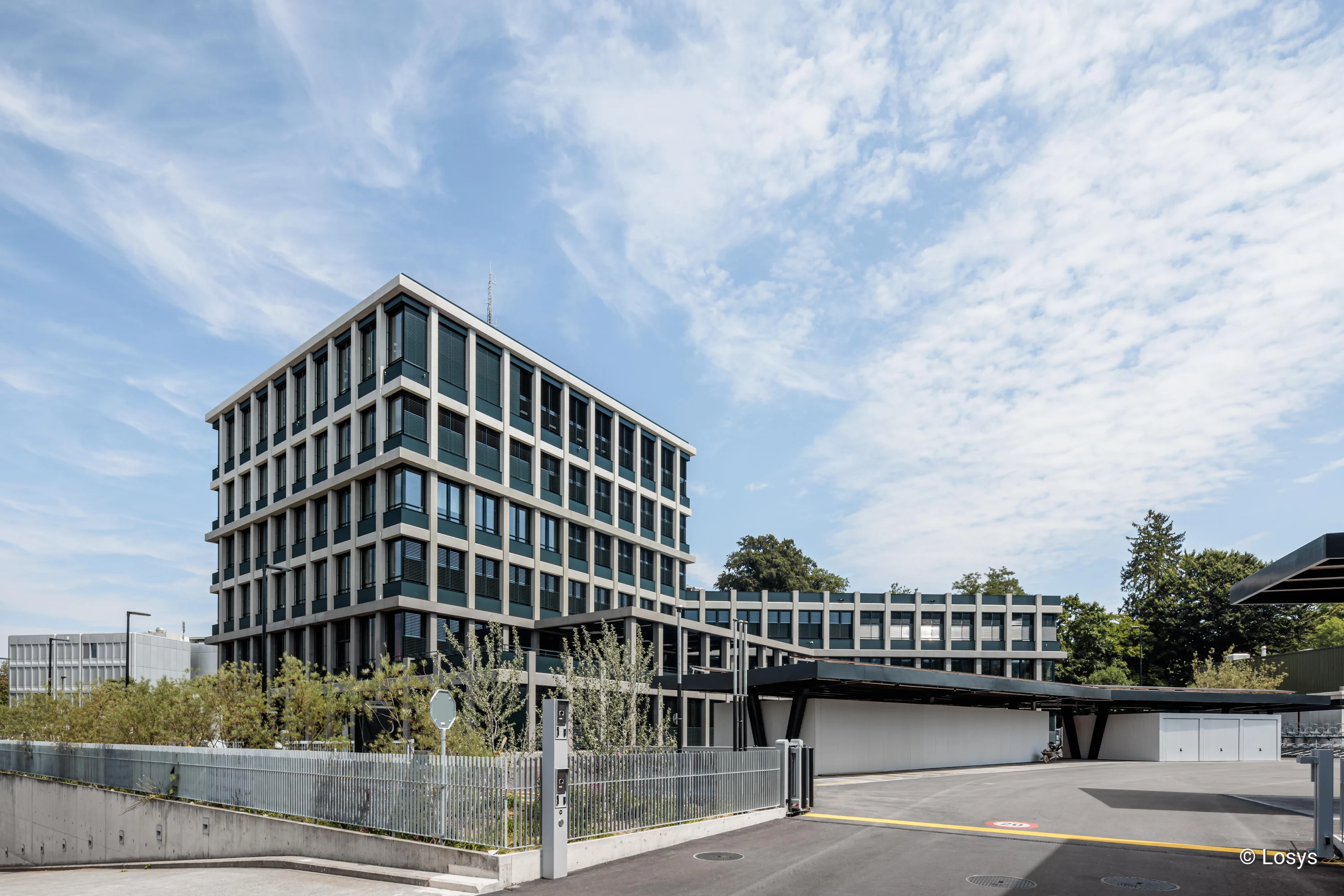 Mehrstöckiges Polizeigebäude in Winterthur mit gleichmäßigem Fenster-Raster, überdachtem Nebeneingang, Zufahrt und Metallzaun.